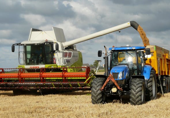 A modern combine harvester and tractor working together to harvest wheat in a sunny outdoor field.