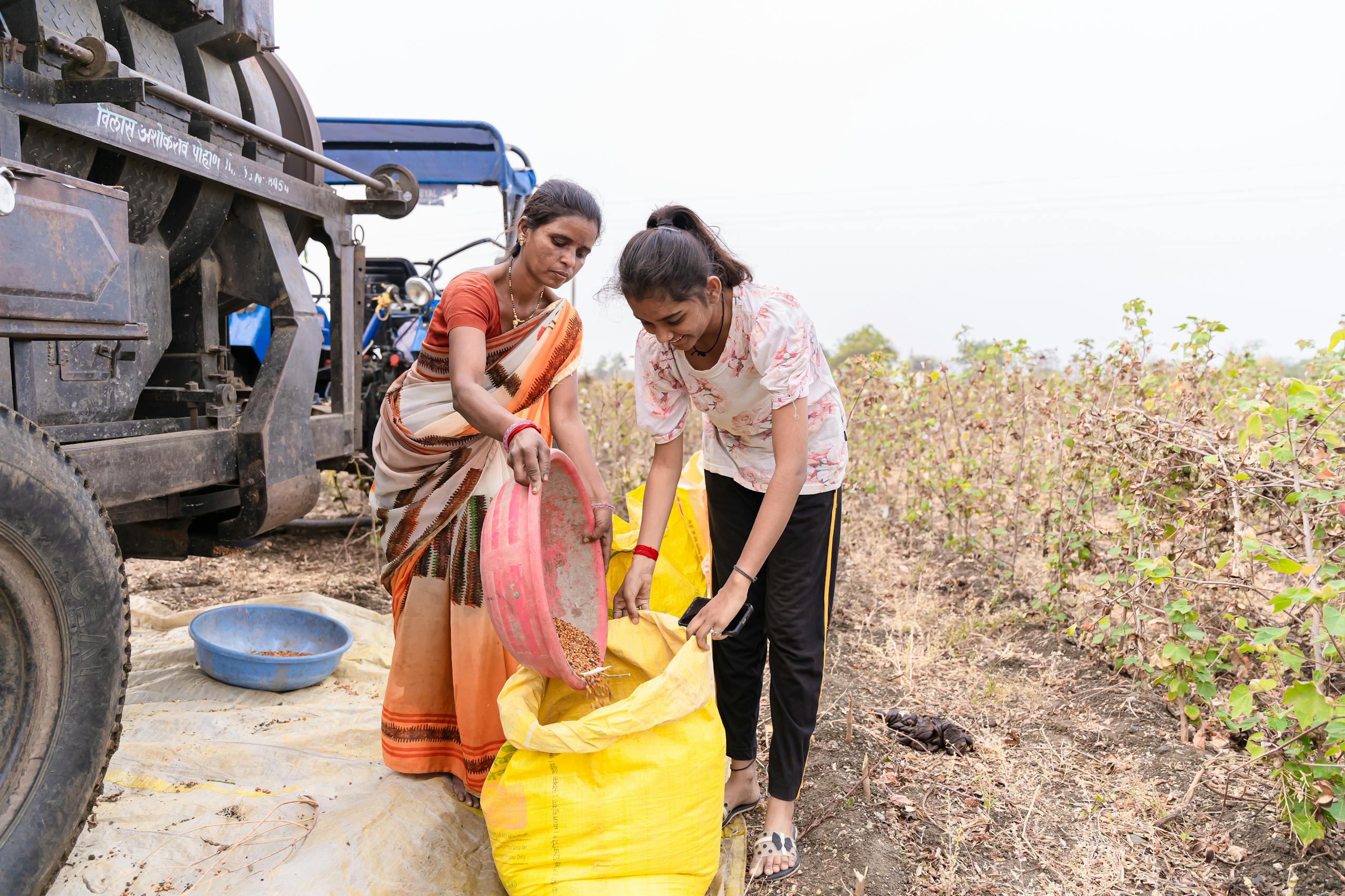Two women harvesting crops in a rural field in Nagpur, India, with traditional tools and attire.