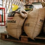 Burlap sacks of coffee beans stacked on a wooden pallet in an industrial warehouse setting.